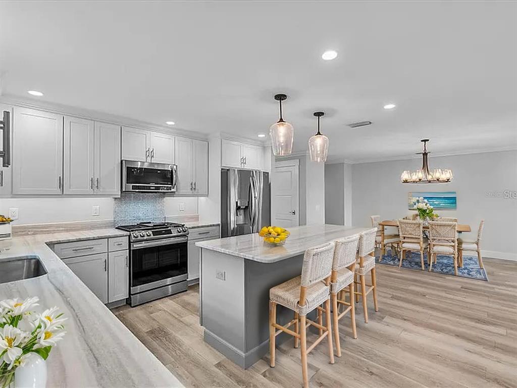 718 Canberra Road Winter Haven, FL 33884 - Photo 3 of 36 a kitchen with stainless steel appliances kitchen island granite countertop a stove a sink a refrigerator a microwave oven a dining table and chairs with wooden floor