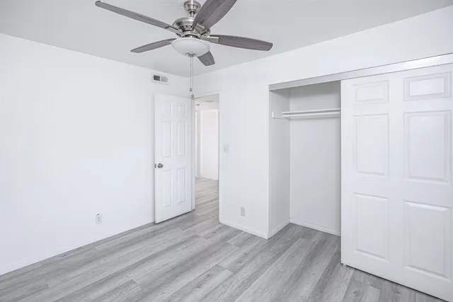 an empty room with wooden floor ceiling fan and windows