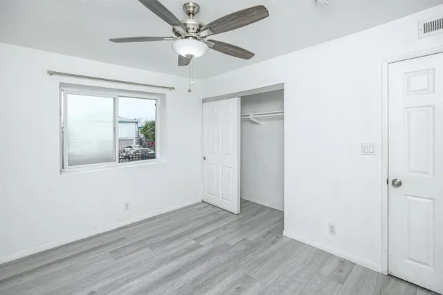 an empty room with wooden floor chandelier fan and windows