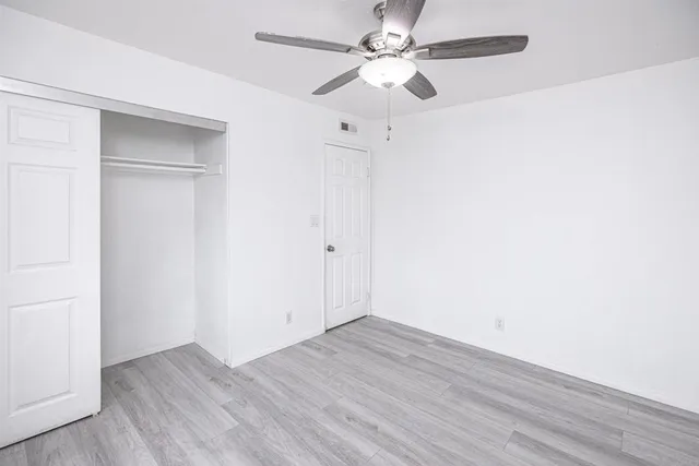 an empty room with wooden floor fan and windows