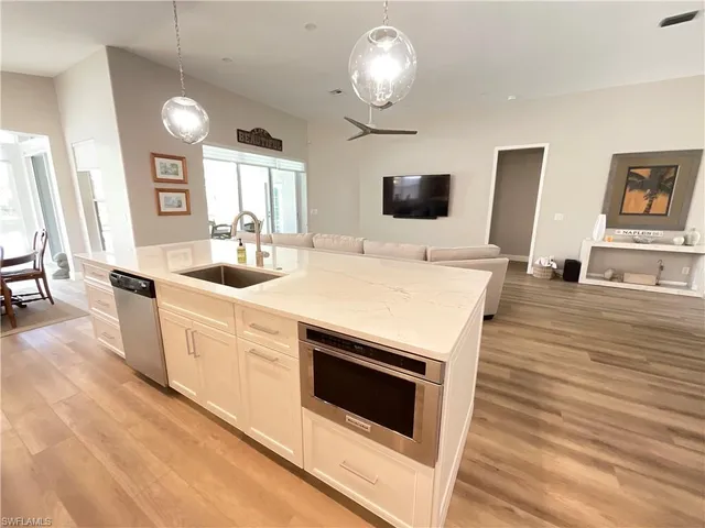 a large white kitchen with sink a microwave a stove and white countertops with wooden floor