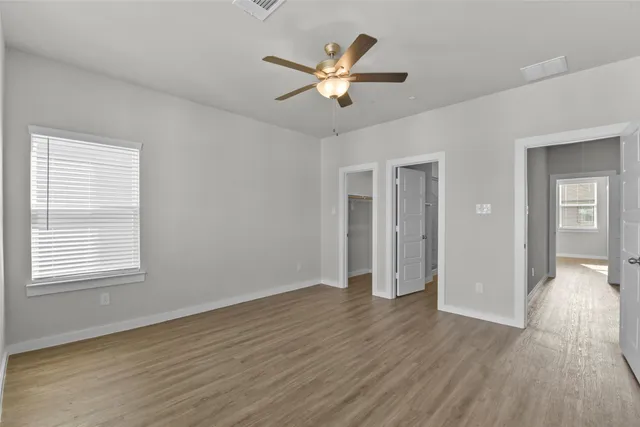 a view of an empty room with wooden floor and a ceiling fan
