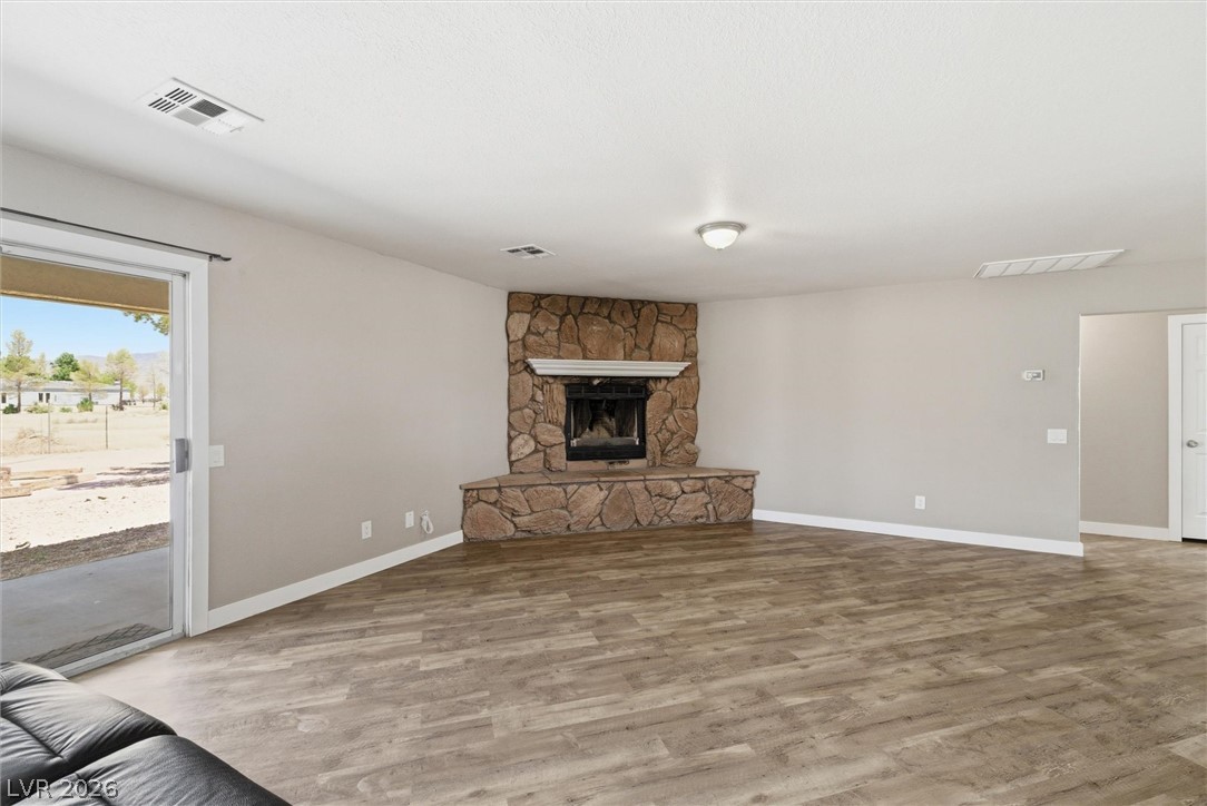 2780 West Simkins Road Pahrump, NV 89060 - Photo 11 of 40 A spacious living area features a charming corner fireplace with a natural stone hearth, complemented by wood flooring.