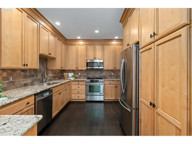 a kitchen with stainless steel appliances granite countertop a refrigerator a sink dishwasher a stove and white cabinets with wooden floor