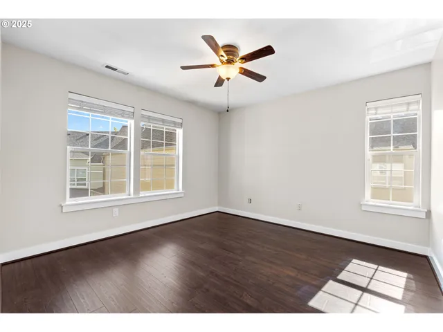 an empty room with wooden floor fan and windows