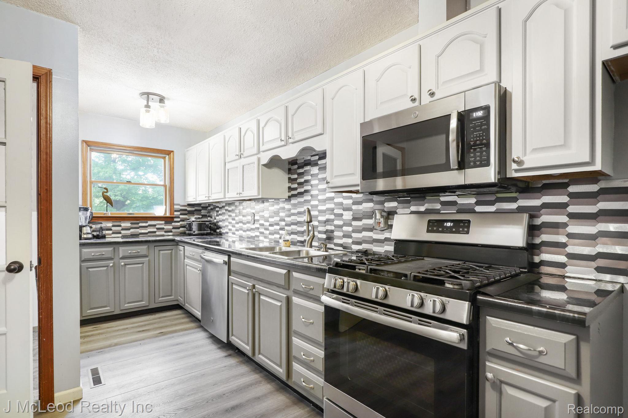 69 West Snover Road Mayville, MI 48744 - Photo 13 of 46 Two-tone cabinetry with stainless steel appliances, black countertops, and a decorative tile backsplash