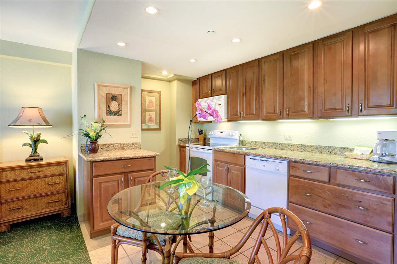 3445 Lower Honoapiilani Road, Unit 336 Lahaina, HI 96761 - Photo 2 of 22 a kitchen with granite countertop wooden cabinets a dining table and chairs with wooden floor