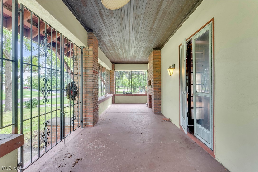 17406 Nottingham Road Cleveland, OH 44119 - Photo 9 of 45 Expansive covered porch featuring a wood-panel ceiling, brick accents, wrought iron fencing, a wall-mounted light fixture, and a set of glass-panel doors
