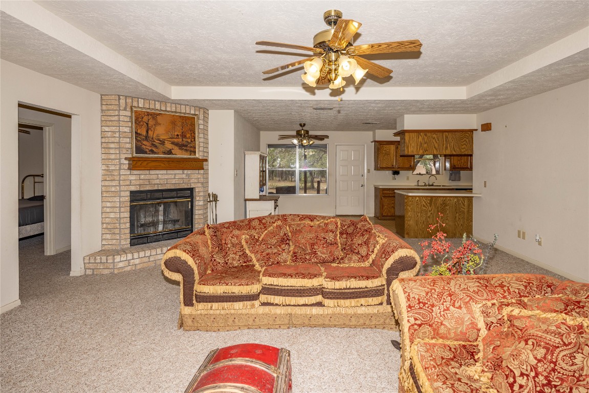 2501 Fischer Store Road Wimberley, TX 78676 - Photo 14 of 37 Living room featuring a raised ceiling, light carpet, a textured ceiling, a brick fireplace, and a ceiling fan