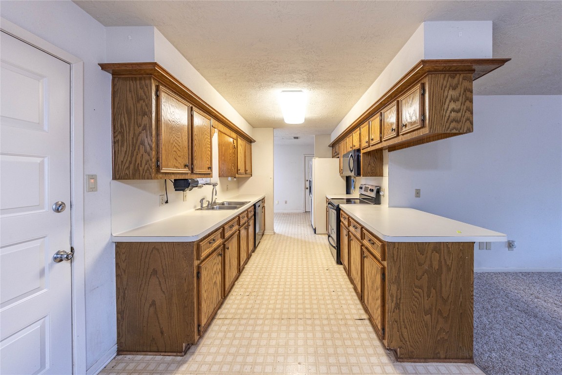 2501 Fischer Store Road Wimberley, TX 78676 - Photo 17 of 37 Kitchen with light floors, brown cabinetry, black appliances, and light countertops