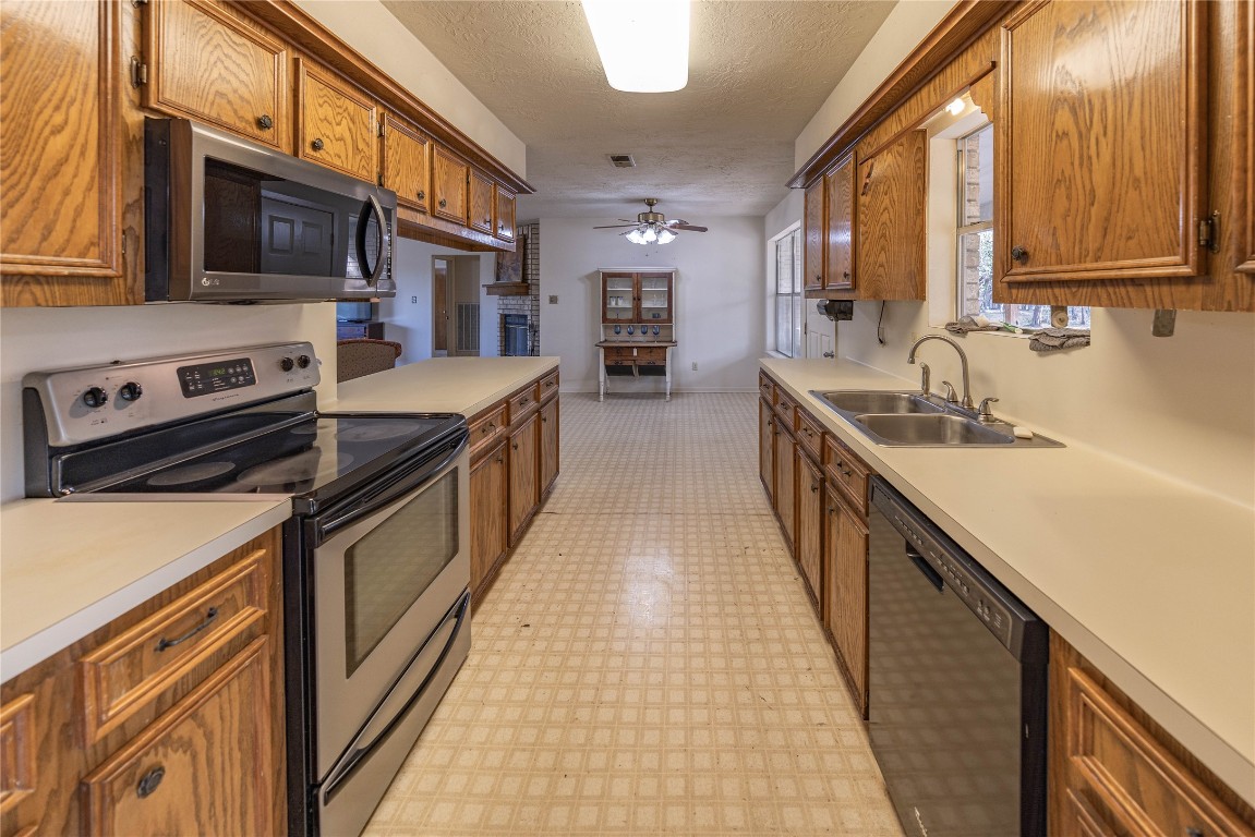 2501 Fischer Store Road Wimberley, TX 78676 - Photo 18 of 37 Kitchen featuring stainless steel appliances, light flooring, brown cabinetry, light countertops, and a textured ceiling