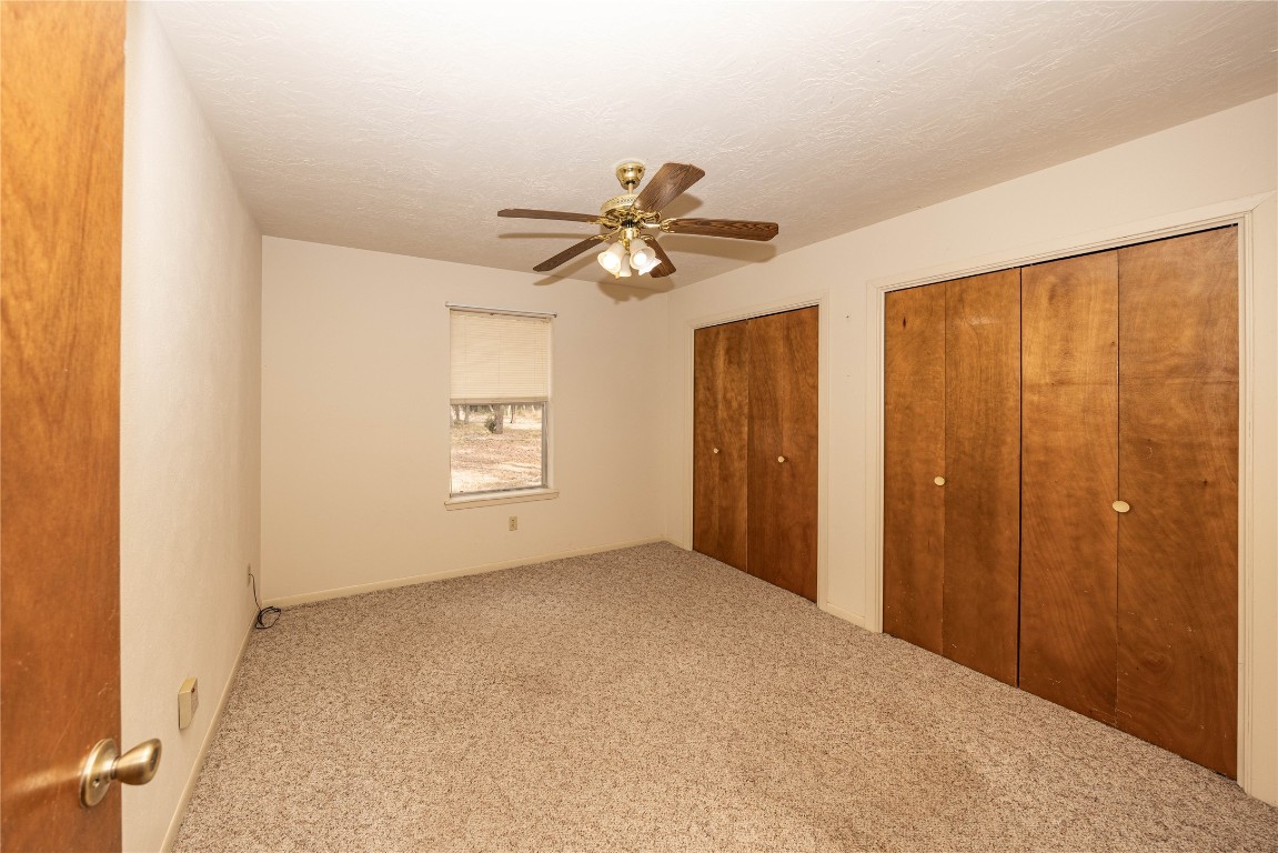 2501 Fischer Store Road Wimberley, TX 78676 - Photo 25 of 37 Unfurnished bedroom featuring two closets, carpet, a textured ceiling, and ceiling fan