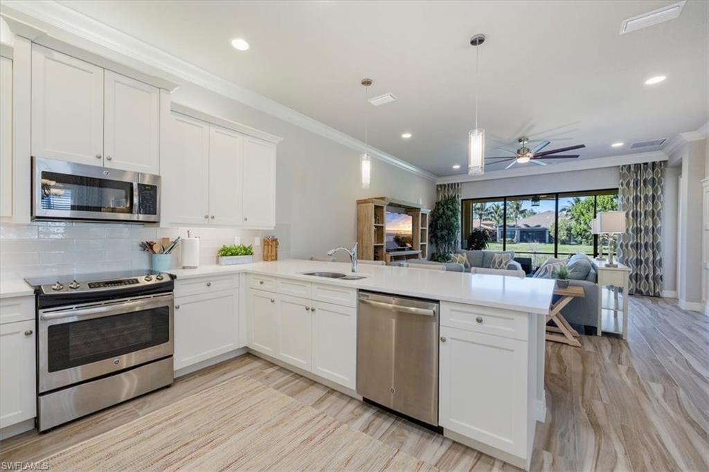 13422 Silktail Drive Naples, FL 34109 - Photo 8 of 37 Kitchen with a peninsula, a sink, decorative backsplash, light countertops, and stainless steel appliances