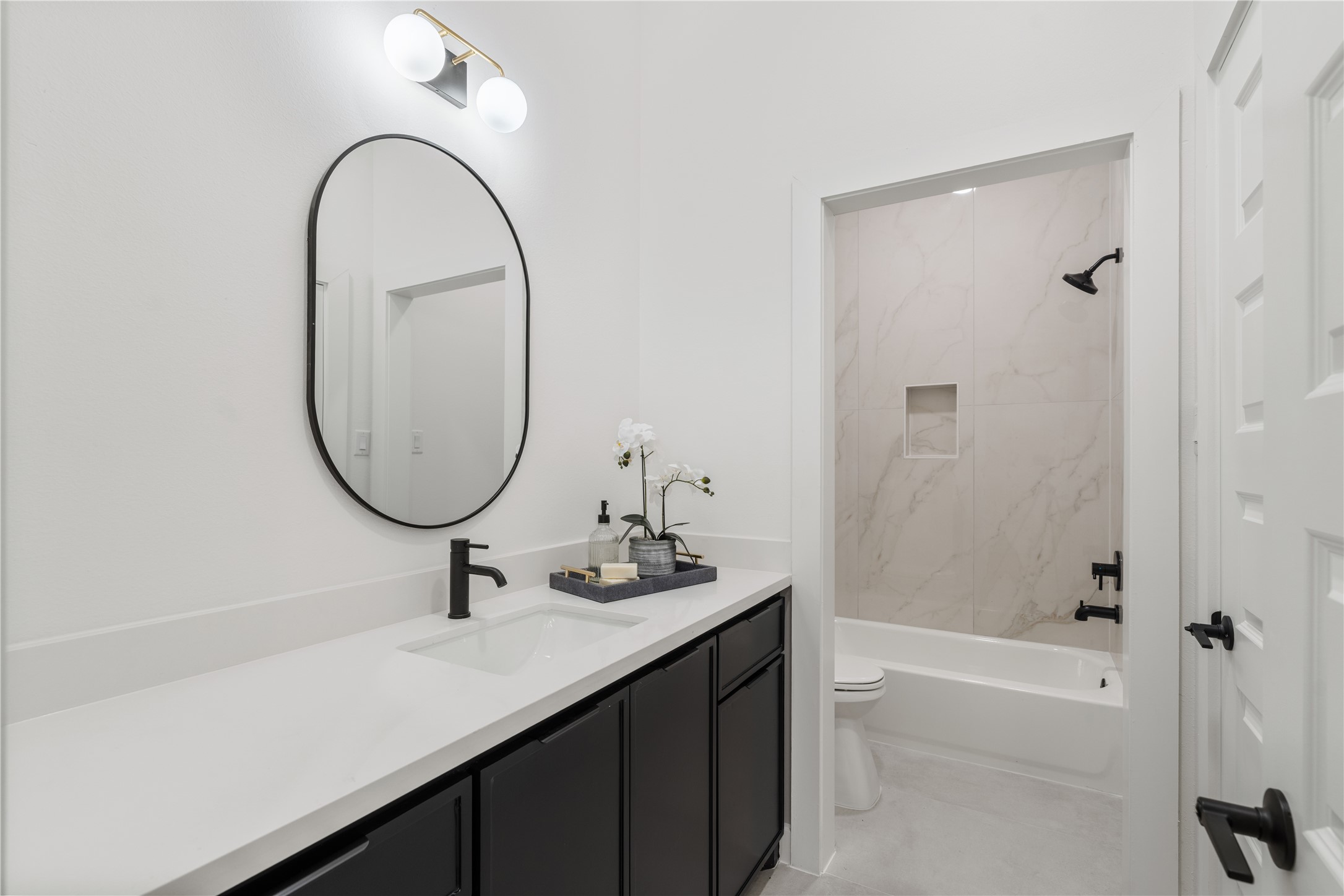 7319 Laura Koppe Road Houston, TX 77028 - Photo 30 of 42 Sleek modern bathroom featuring a chic black vanity with dual sinks, an elegant oval mirror, and a bathtub with stylish marble-look tile.