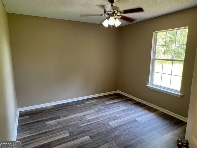 an empty room with wooden floor fan and windows