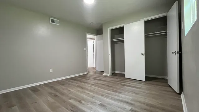 a view of an empty room with wooden floor and closet