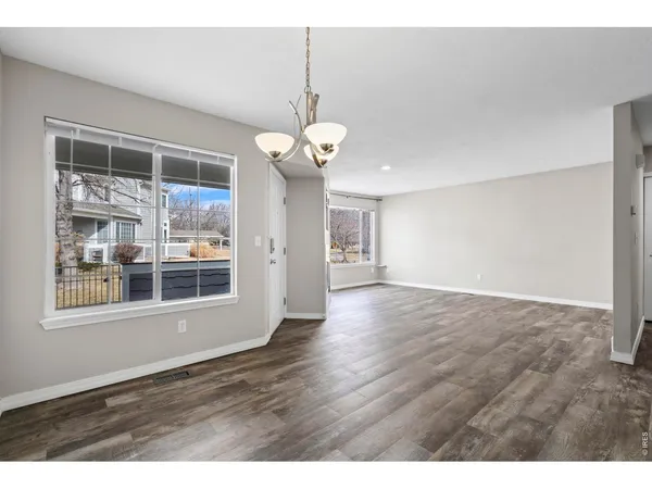 a view of an empty room with wooden floor and a kitchen