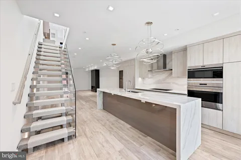 a large white kitchen with wooden floors stainless steel appliances and a chandelier