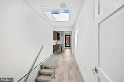 a hallway with wooden floor staircase and a kitchen view