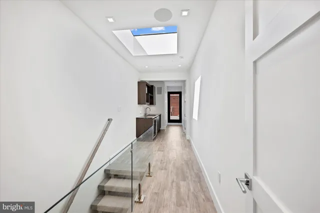 a hallway with wooden floor staircase and a kitchen view