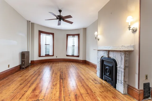 a view of a livingroom with a fireplace a ceiling fan and wooden floor