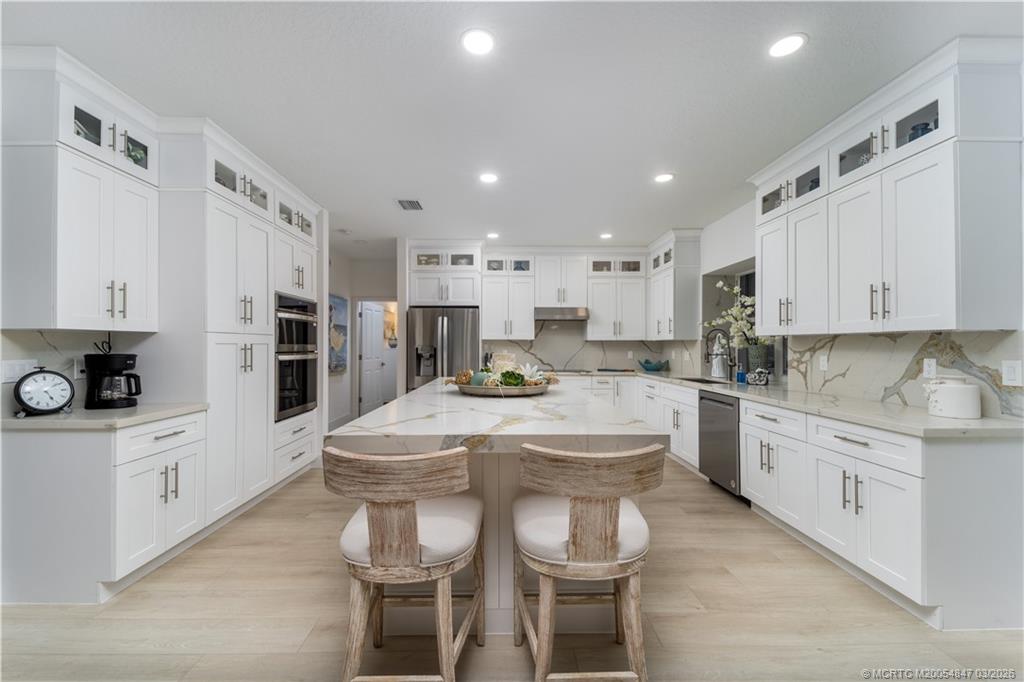 1257 Southeast Brewster Place Stuart, FL 34997 - Photo 14 of 35 a kitchen with stainless steel appliances kitchen island granite countertop a table chairs sink and cabinets