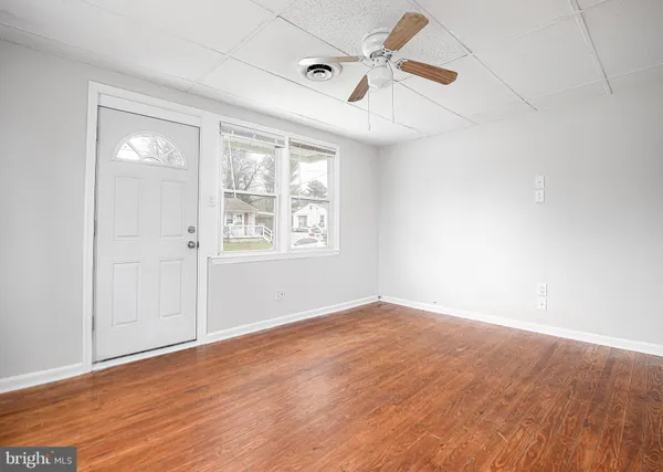 an empty room with wooden floor ceiling fan and windows