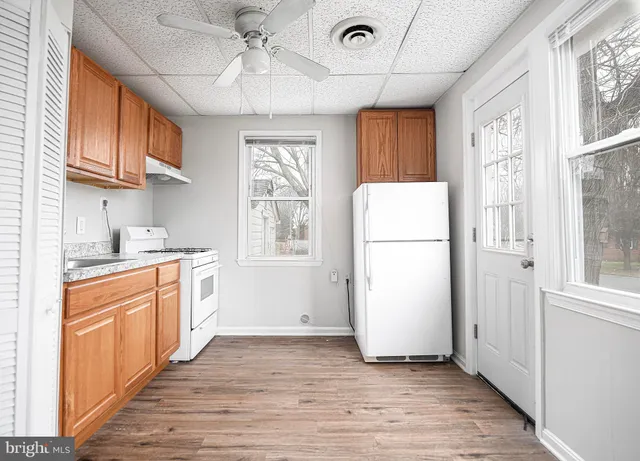 a kitchen with stainless steel appliances granite countertop a refrigerator a microwave oven a sink and white cabinets with wooden floor