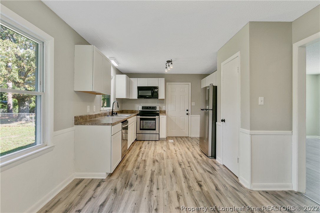 711 Bronco Road Fayetteville, NC 28303 - Photo 12 of 42 a kitchen with granite countertop a refrigerator a sink dishwasher a stove and white cabinets with wooden floor