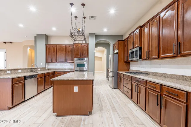 a large kitchen with stainless steel appliances granite countertop a stove a sink dishwasher a refrigerator and wooden cabinets with wooden floor
