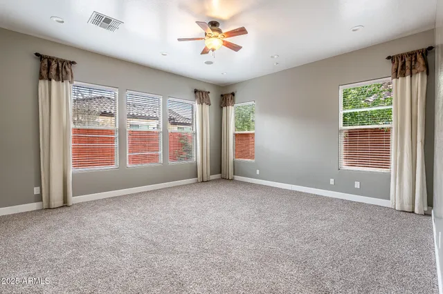 an empty room with chandelier fan and windows