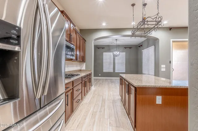 a kitchen with stainless steel appliances granite countertop a refrigerator a sink dishwasher a stove and a dining table with wooden floor