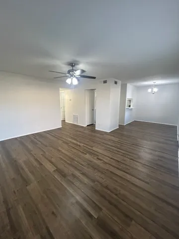 a view of an empty room with wooden floor and a ceiling fan