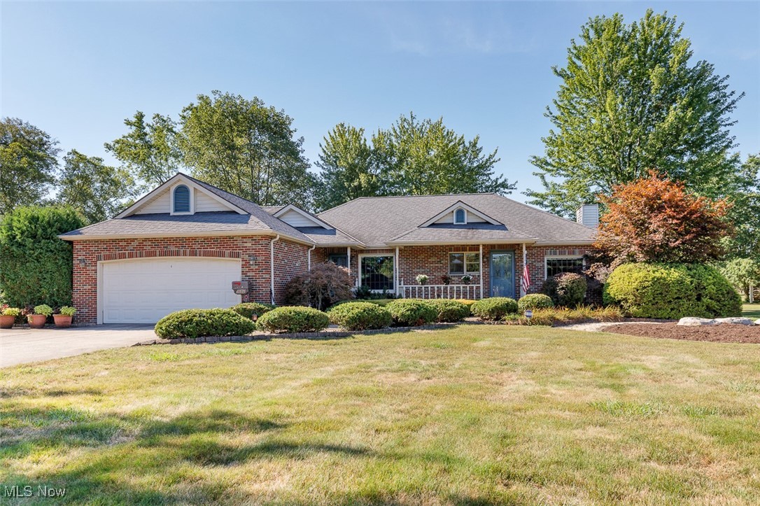 Front view of home with a covered porch, brick siding, driveway, a garage, and a front landscaped yard