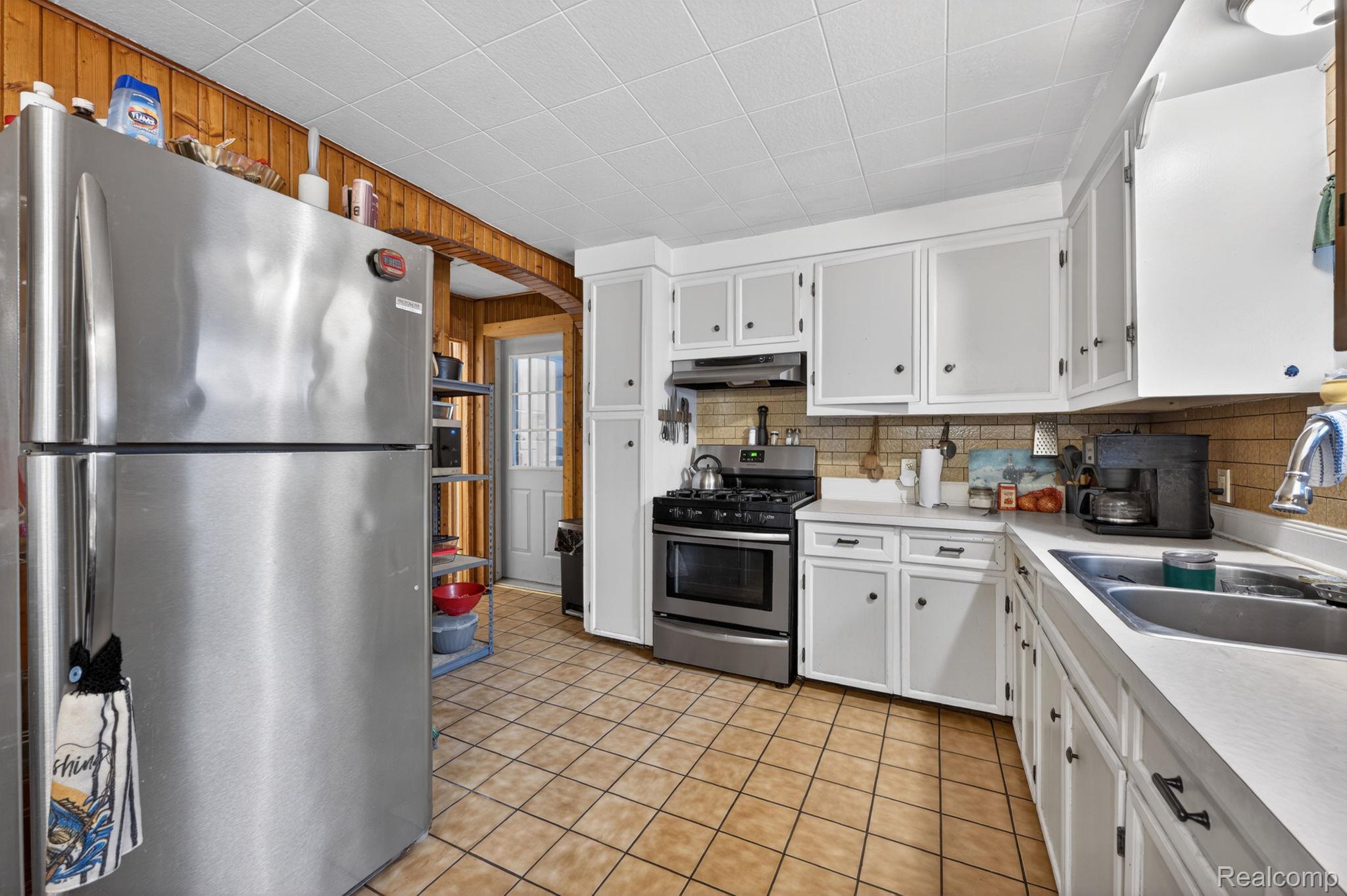 304 West Ridge Street Owosso, MI 48867 - Photo 17 of 45 Kitchen featuring stainless steel appliances, light countertops, white cabinetry, wood walls, and arched walkways