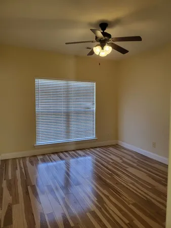 a view of an empty room with wooden floor and a fan