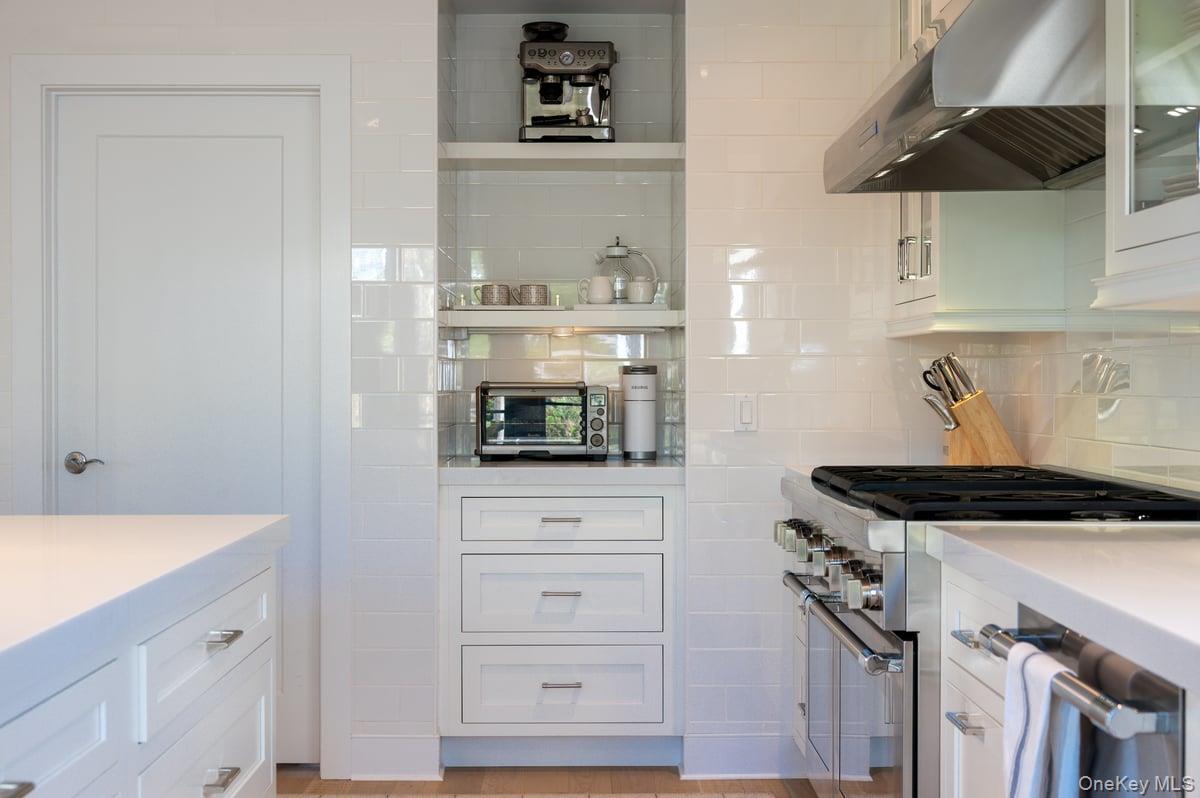 1 Primrose Lane Rye Brook, NY 10573 - Photo 10 of 42 Kitchen with white cabinets, under cabinet range hood, high end stainless steel range oven, decorative backsplash, and light stone countertops