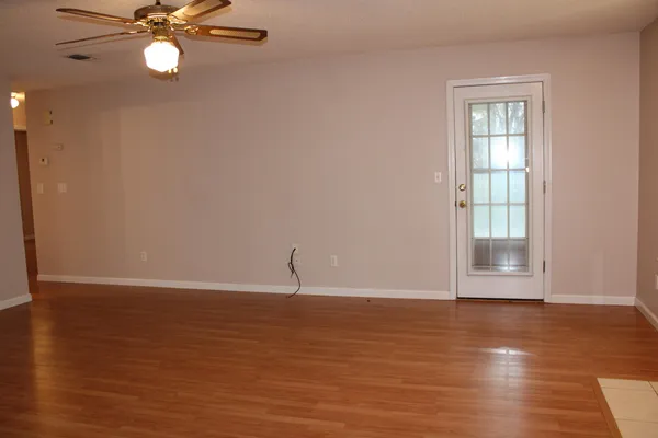 a view of an empty room with wooden floor and fan