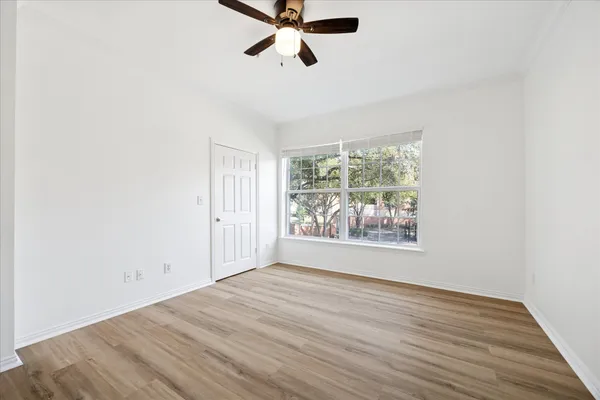 an empty room with wooden floor fan and windows