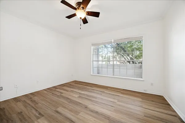 an empty room with wooden floor fan and windows