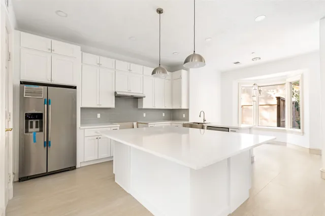 a large kitchen with stainless steel appliances granite countertop a sink a refrigerator a stove and white cabinets with wooden floor