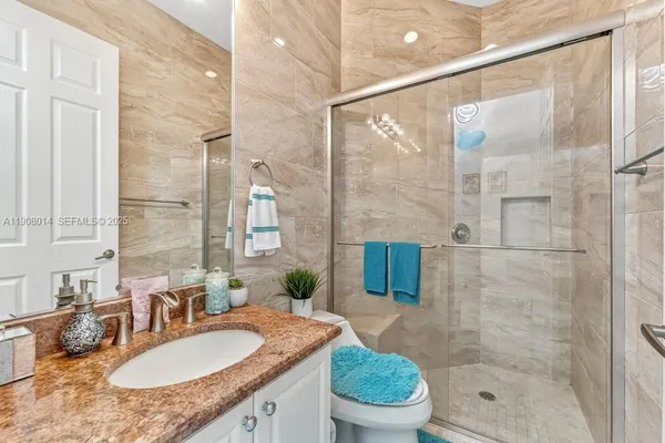 a bathroom with a granite countertop sink a toilet a mirror and shower
