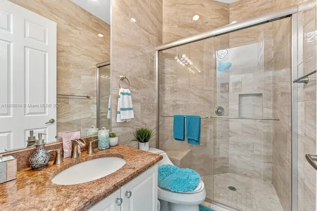 a bathroom with a granite countertop sink a toilet a mirror and shower