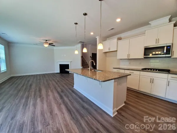 a kitchen with kitchen island granite countertop a sink a microwave oven a stove and white cabinets with wooden floor