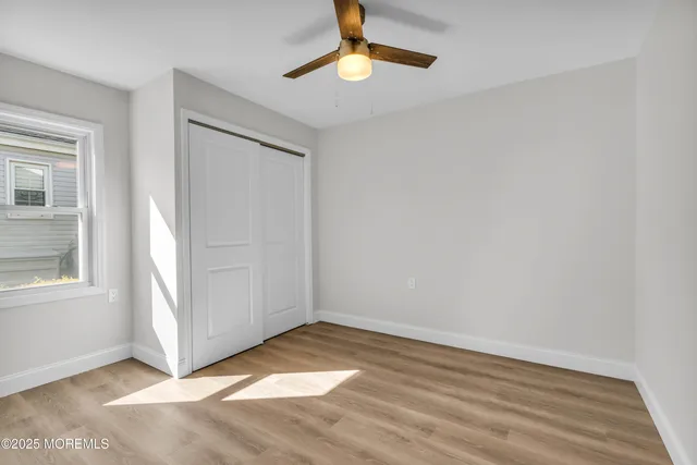an empty room with wooden floor chandelier fan and windows