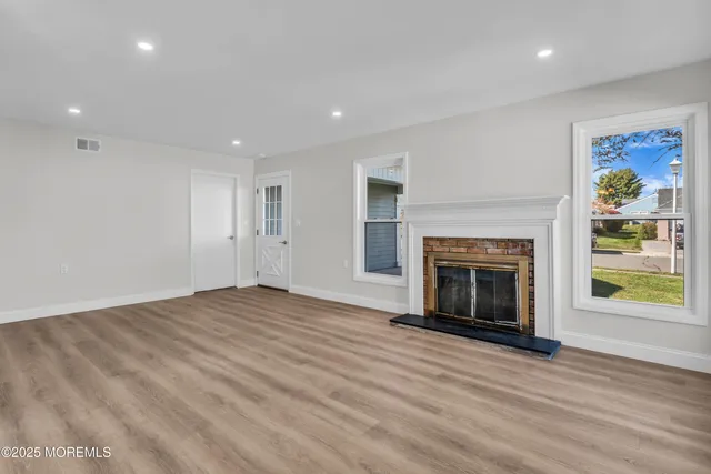 a view of an empty room with wooden floor fireplace and a window