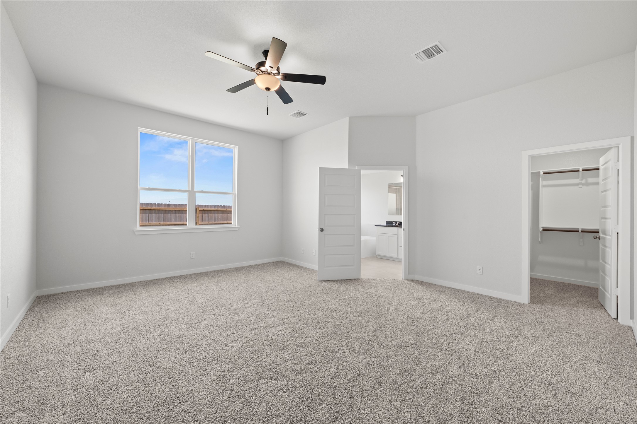 220 Gus Loop Georgetown, TX 78626 - Photo 10 of 18 A spacious, naturally illuminated bedroom features soft carpeting, a ceiling fan, and access to an en-suite bathroom and walk-in closet.