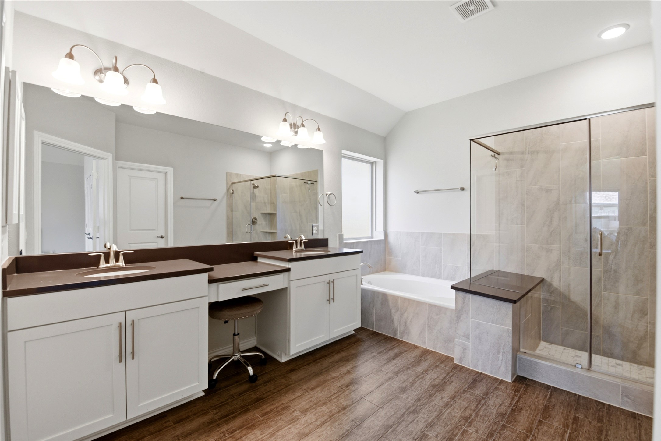 17834 Maple Ash Drive Spring, TX 77379 - Photo 22 of 50 Primary bathroom includes dual sinks with spacious countertops, a large mirror, a separate shower with glass doors, and a built-in bathtub. The room is well-lit with modern fixtures and has warm wood flooring.