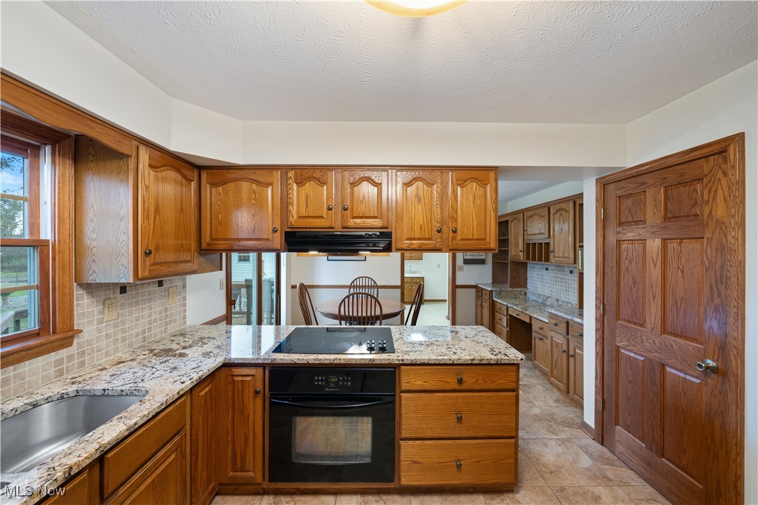 891 Station Road Valley City, OH 44280 - Photo 17 of 45 Kitchen featuring decorative backsplash, a textured ceiling, light stone countertops, black appliances, and ventilation hood