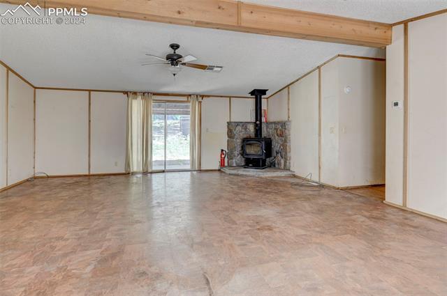 2259 Pathfinder Road Florissant, CO 80816 - Photo 16 of 33 Unfurnished living room with ceiling fan, light tile patterned floors, a wood stove, and a textured ceiling
